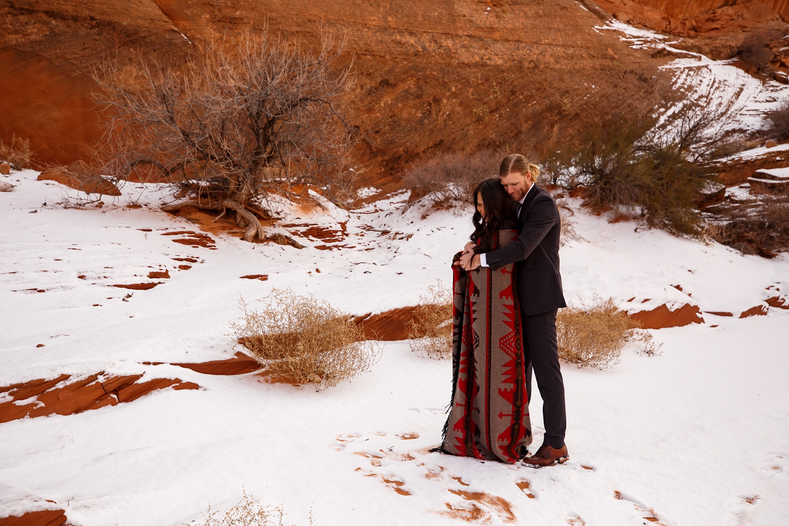 Couple cuddling under a blanket in a snowy slot canyon.