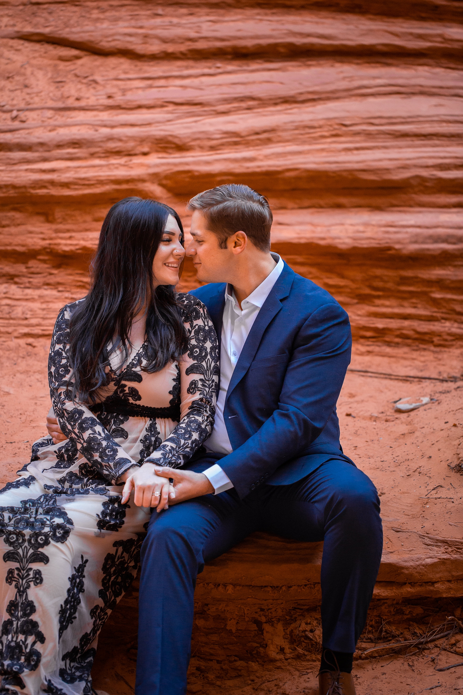 Engaged couple sitting on red rocks in Utah.