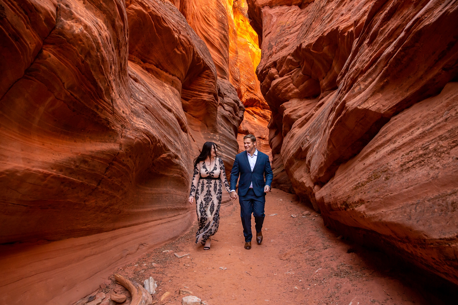 Engaged couple running through a red rock slot canyon