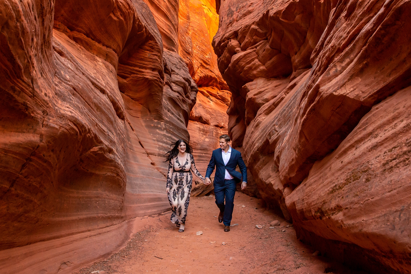 Adventurous engaged couple running through a Utah slot canyon.