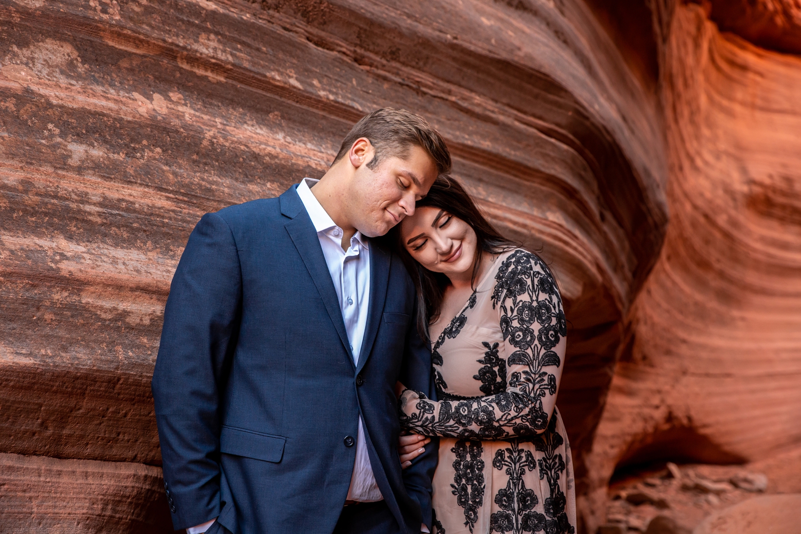 Engaged lovers cuddling in a red rocks slot canyon.