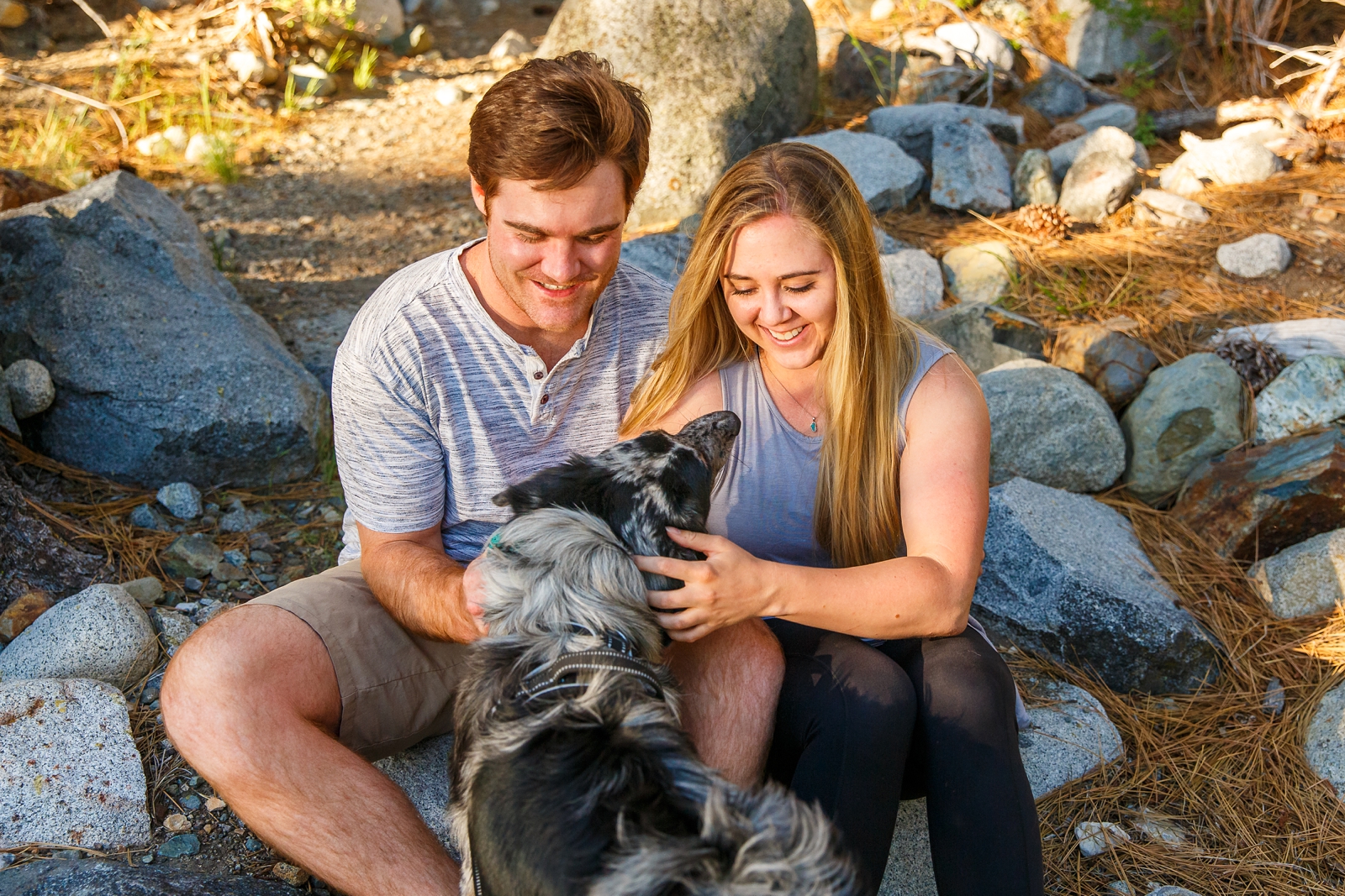 a couple sitting next to each other smiling with their dog by Lake Tahoe for their adventure session