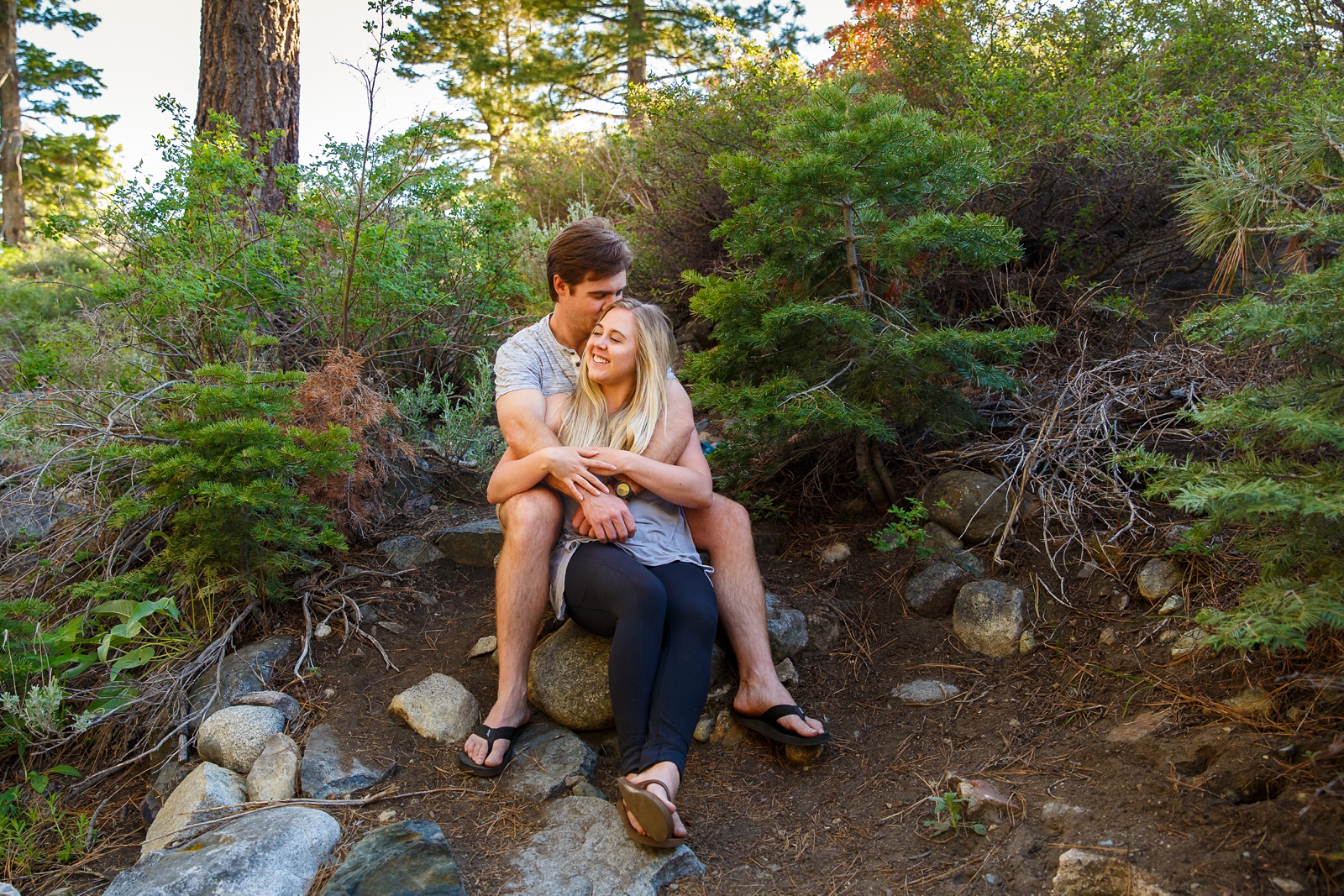 a couple sitting on a rock embracing with the man kissing his girlfriend on the forehead during their Lake Tahoe area adventure session