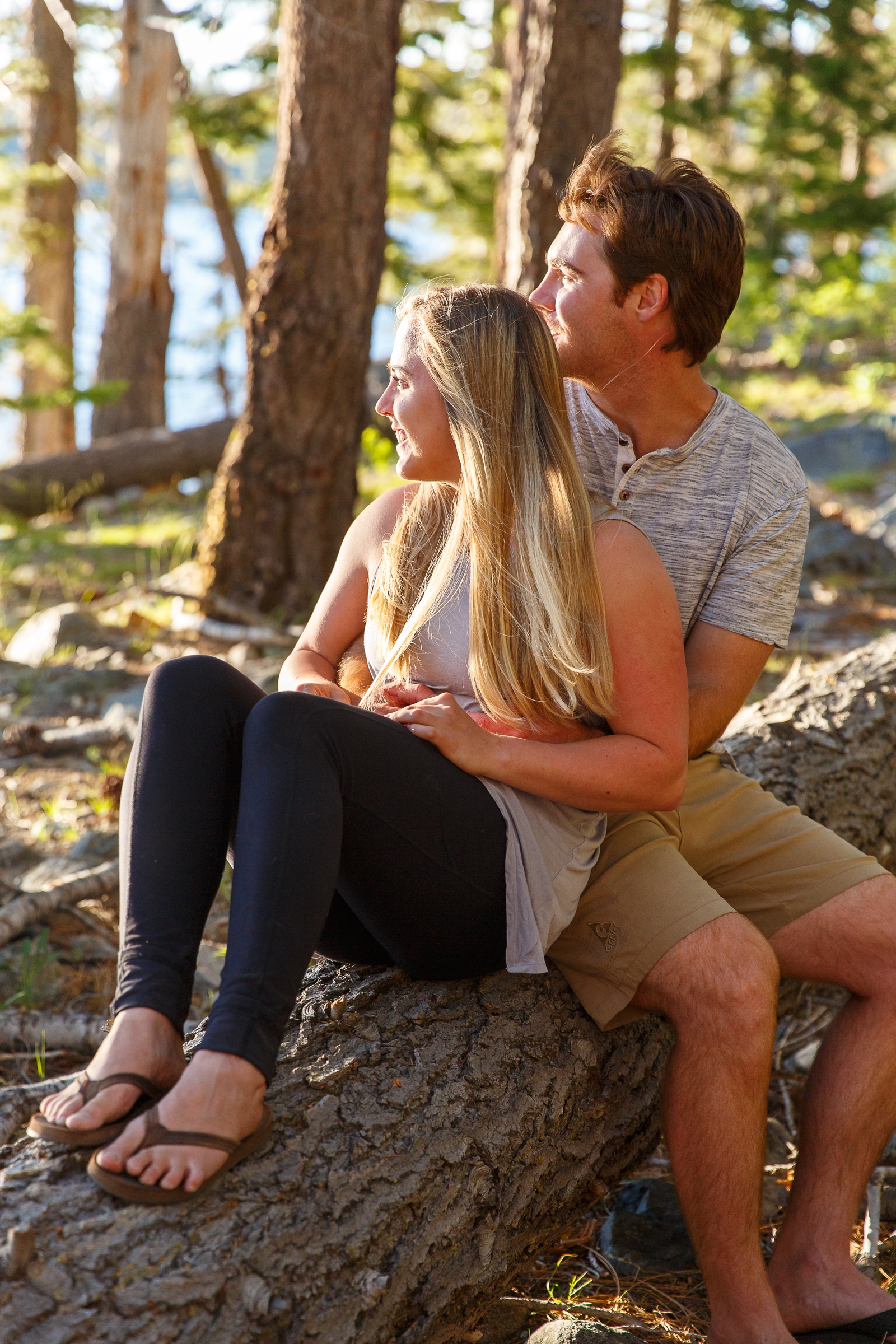 a couple embracing each other sitting on a fallen branch by Lake Tahoe for their adventure session