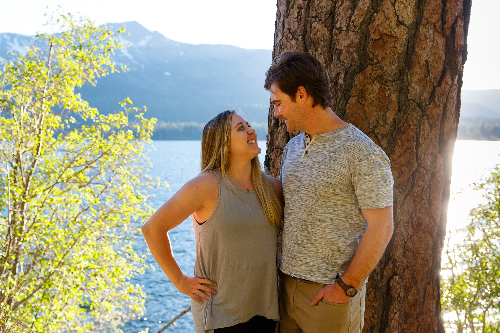a couple smiling at each other in front of a big tree with Lake Tahoe in the background during their adventure session