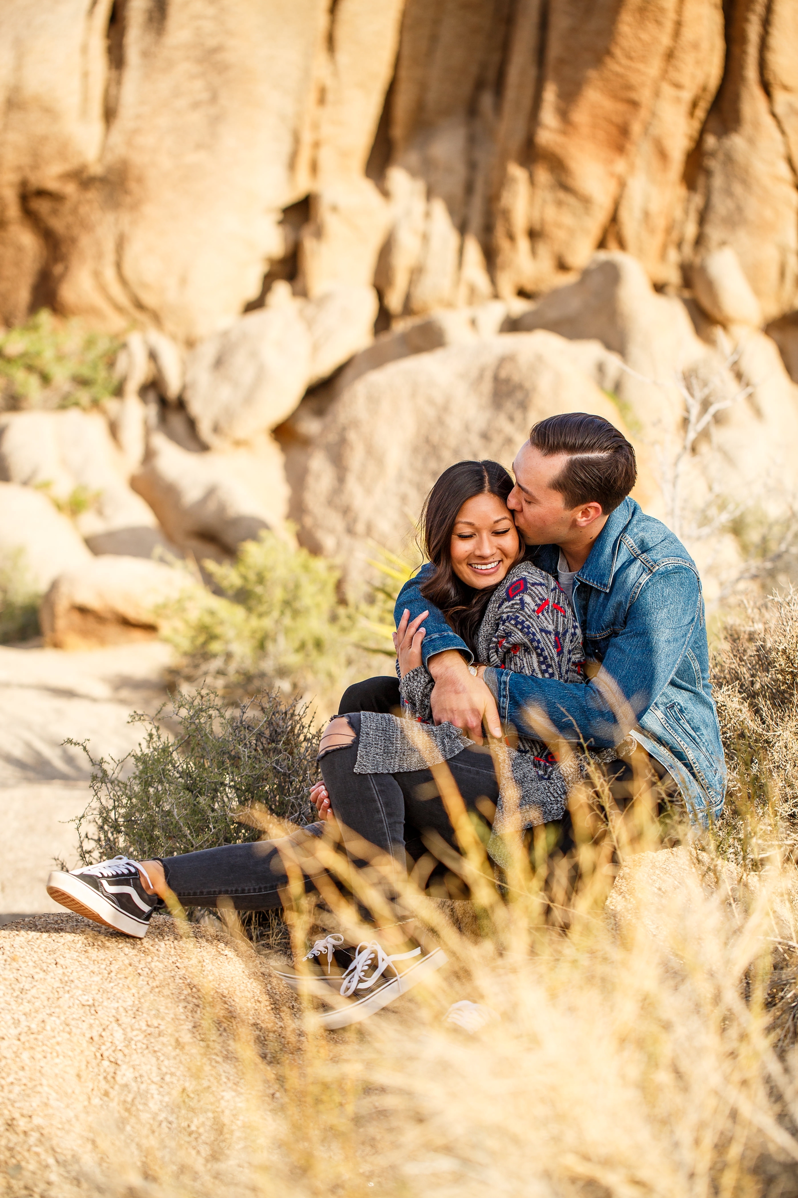 Romantic engaged couple cuddling on boulders in Joshua Tree National Park.
