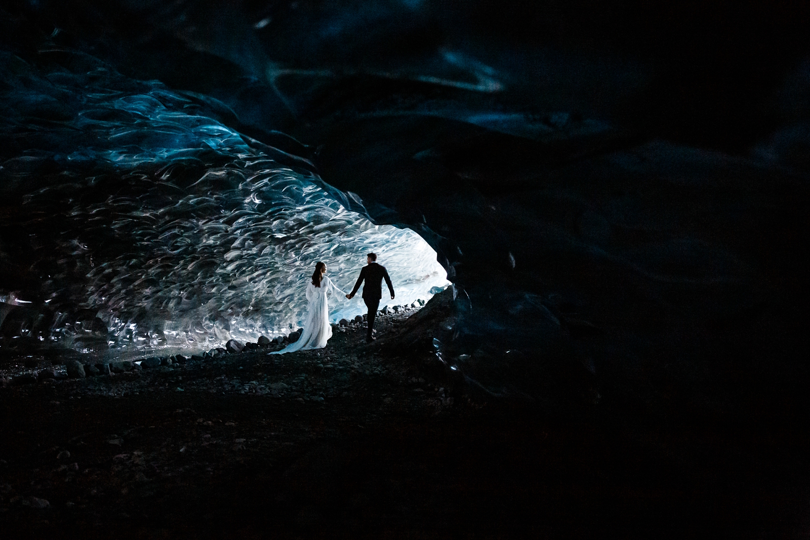 An eloping couple walks through a wintery Iceland ice cave.