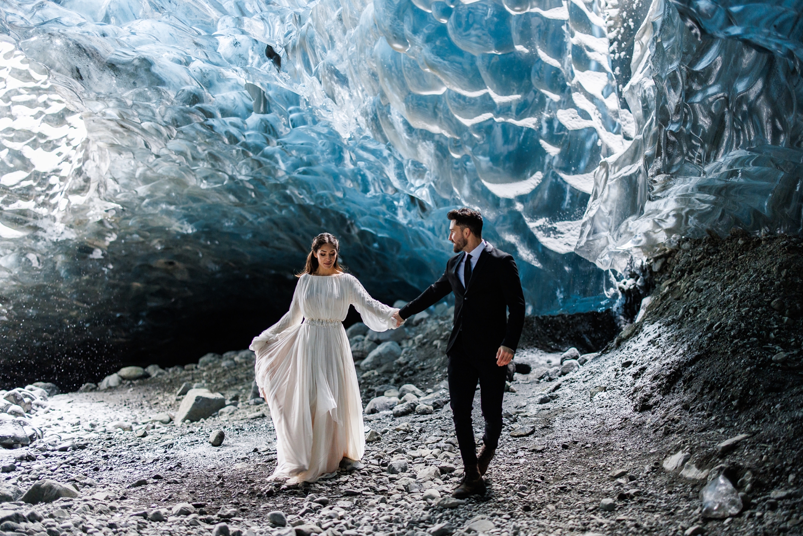 An eloping couple walking in an Iceland ice cave on their wedding day.