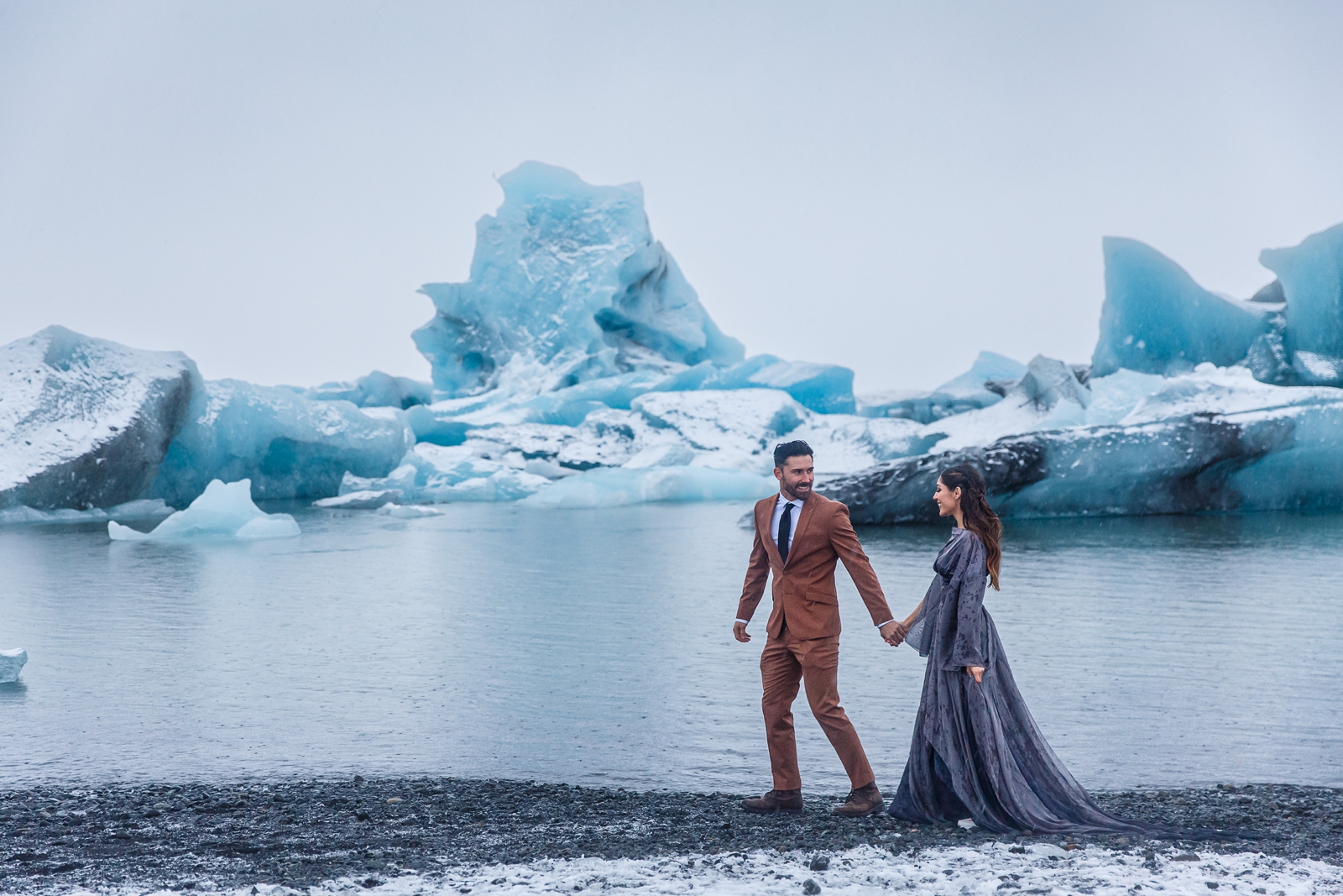 An eloping couple walks along the shore of Jökulsárlón glacier lagoon in Iceland.