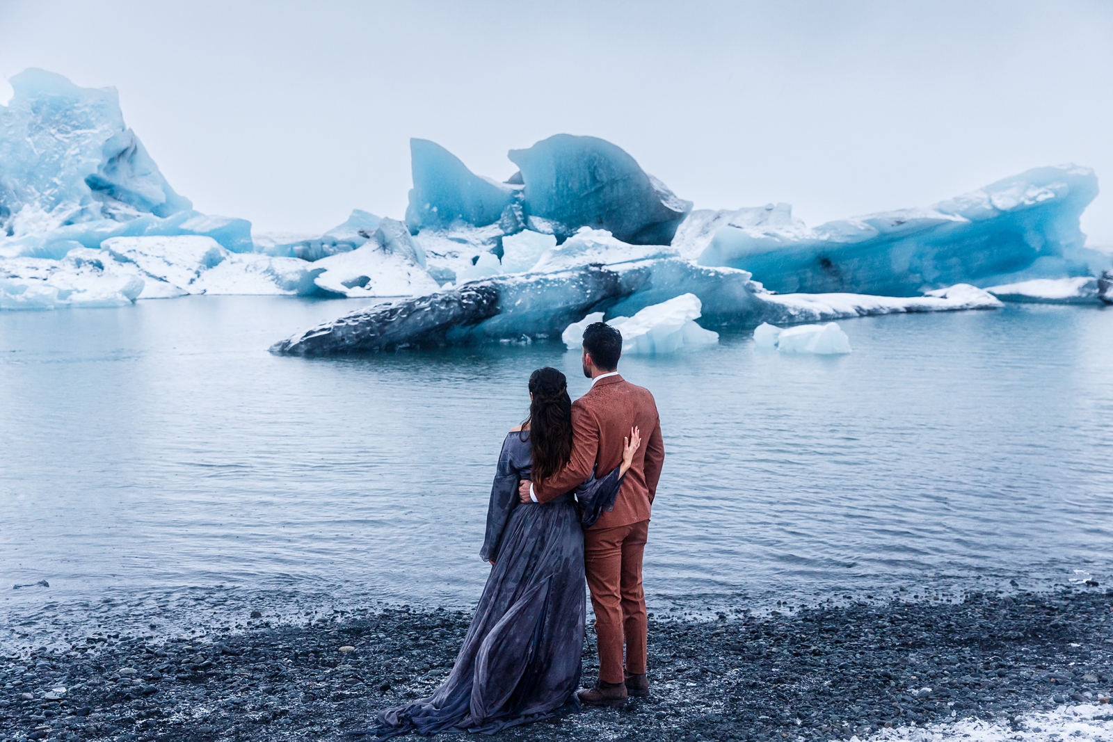 Eloping couple gazing at the otherworldly ice formations in the Jökulsárlón glacier lagoon, Iceland.