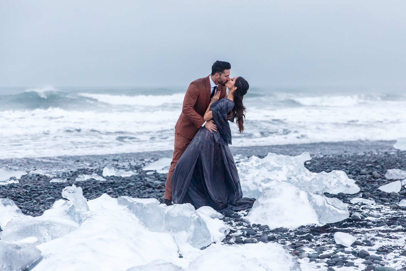 A couple kissing passionately at the moody winter seascape of Diamond Beach, Iceland