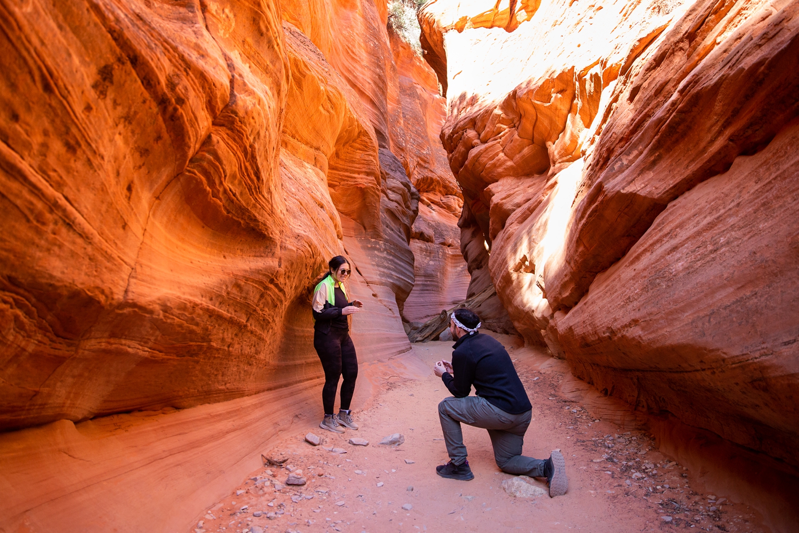 A guy down on his knee proposing to his girlfriend in the middle of the Utah slot canyon during their adventurous hike