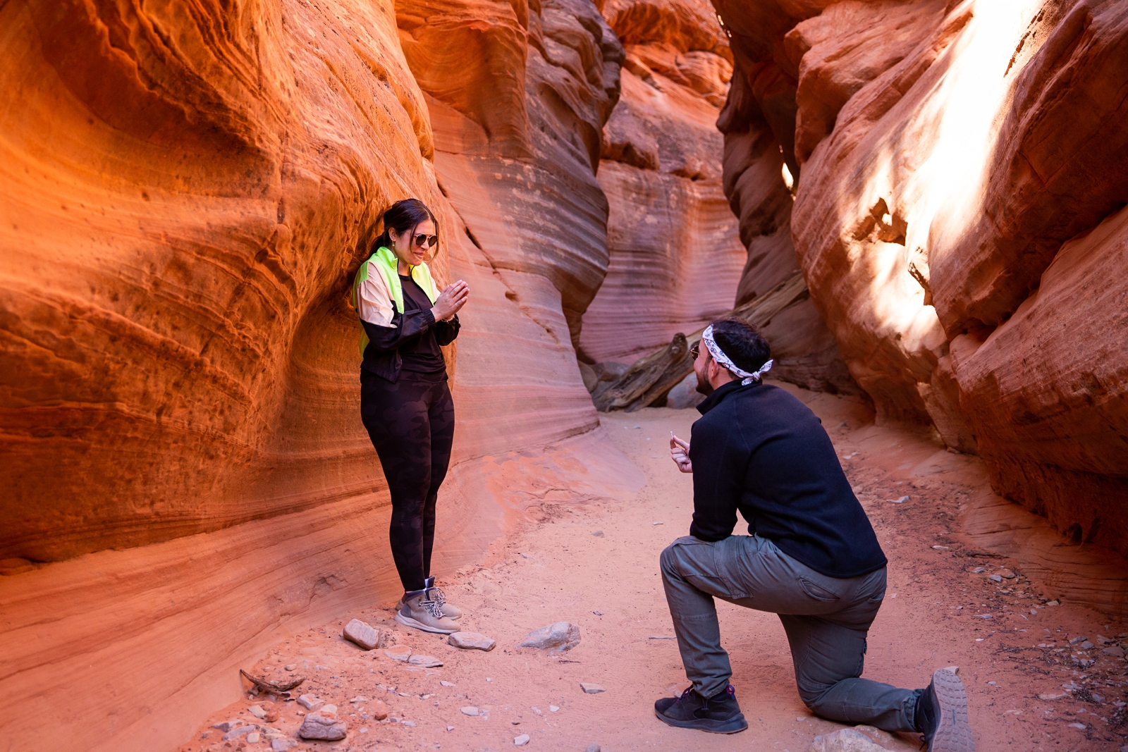 A guy down on his knee proposing to his shocked and surprised girlfriend in the middle of the Utah slot canyon during their adventurous hike
