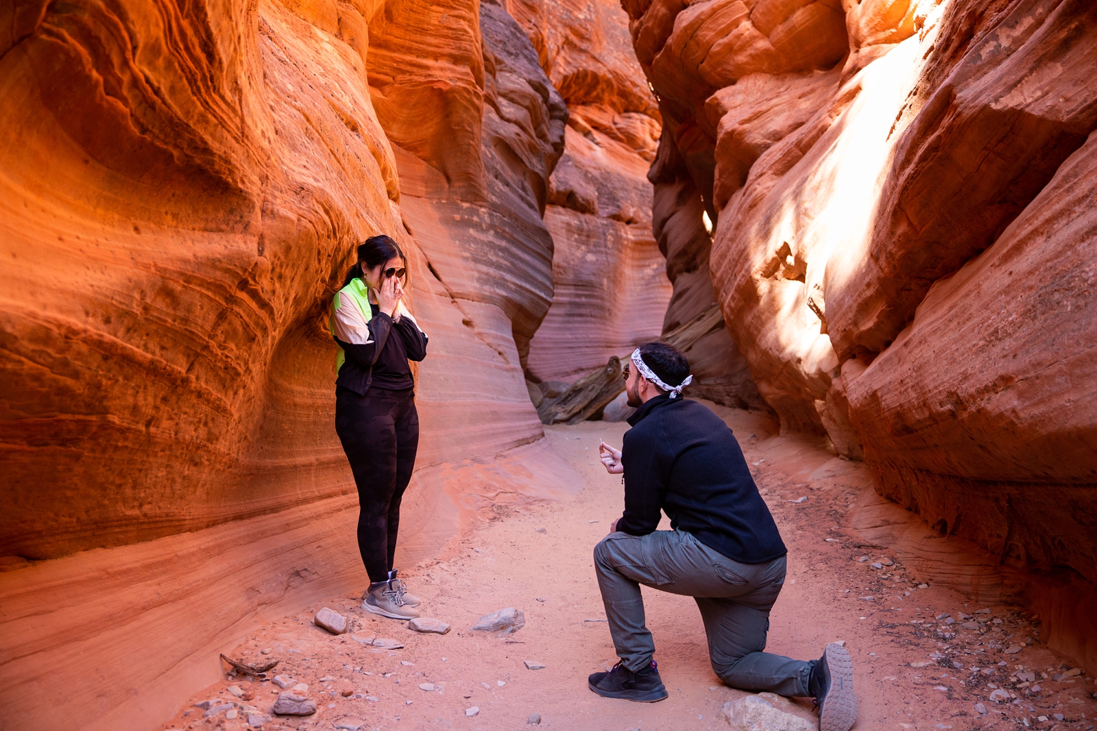 A guy down on his knee proposing to his shocked and surprised girlfriend in the middle of the Utah slot canyon during their adventurous hike