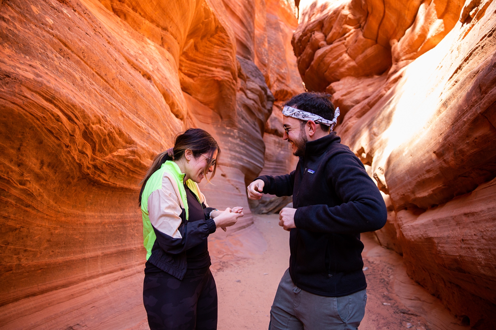 A newly engaged couple looking at each other and the girl is looking at her new ring with a big smile on her face in the Utah slot canyon