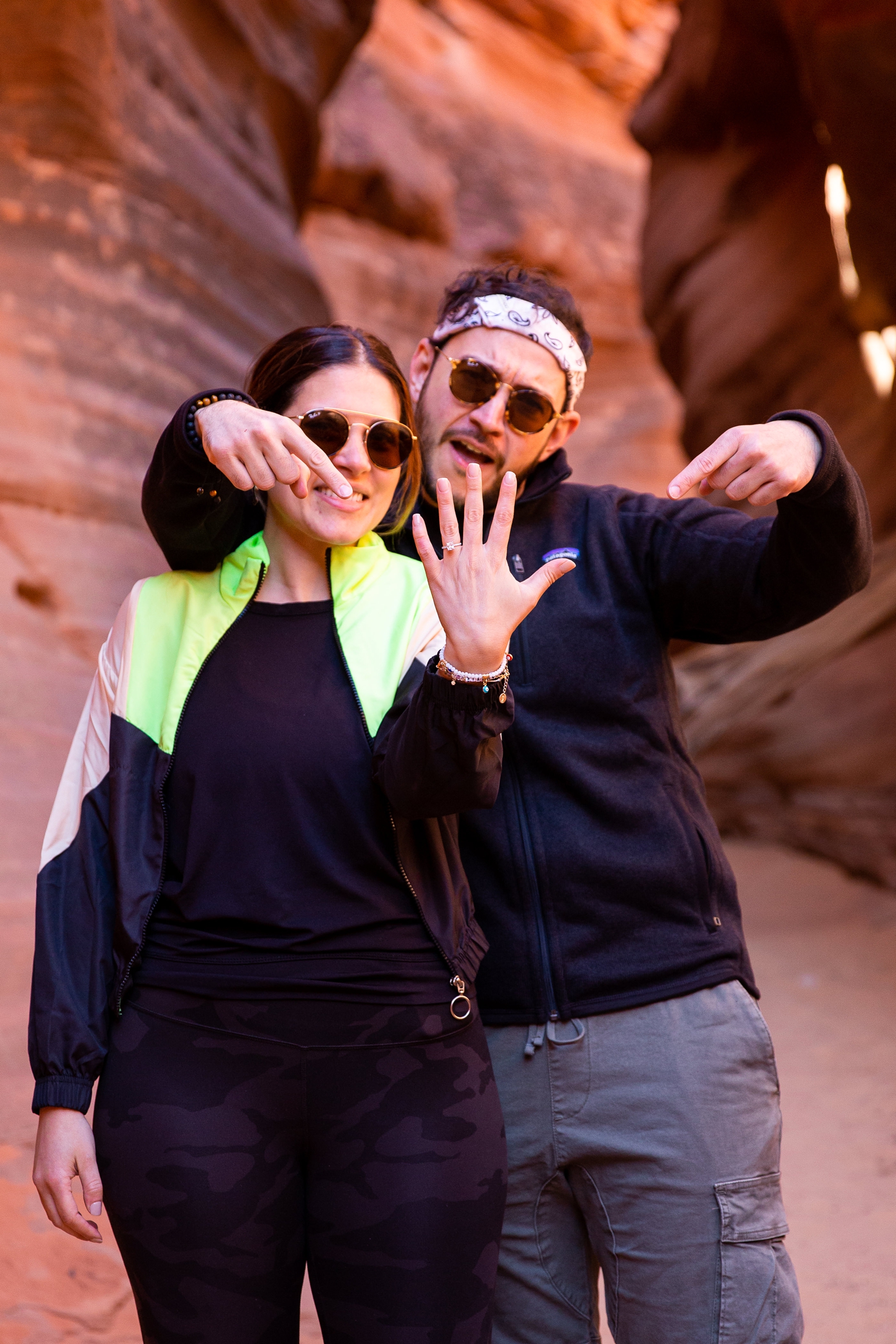 A newly engaged couple posing and smiling showing off the new engagement ring in the Utah Slot Canyon after their surprise adventurous proposal