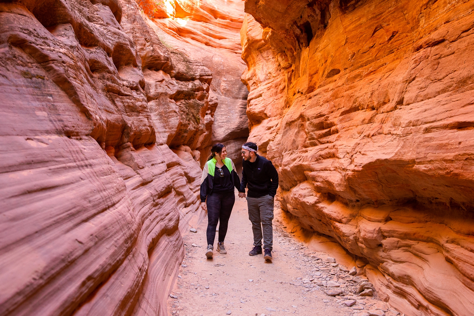 A newly engaged couple walking through the Utah slot canyon holding hands and laughing after their adventurous surprise proposal