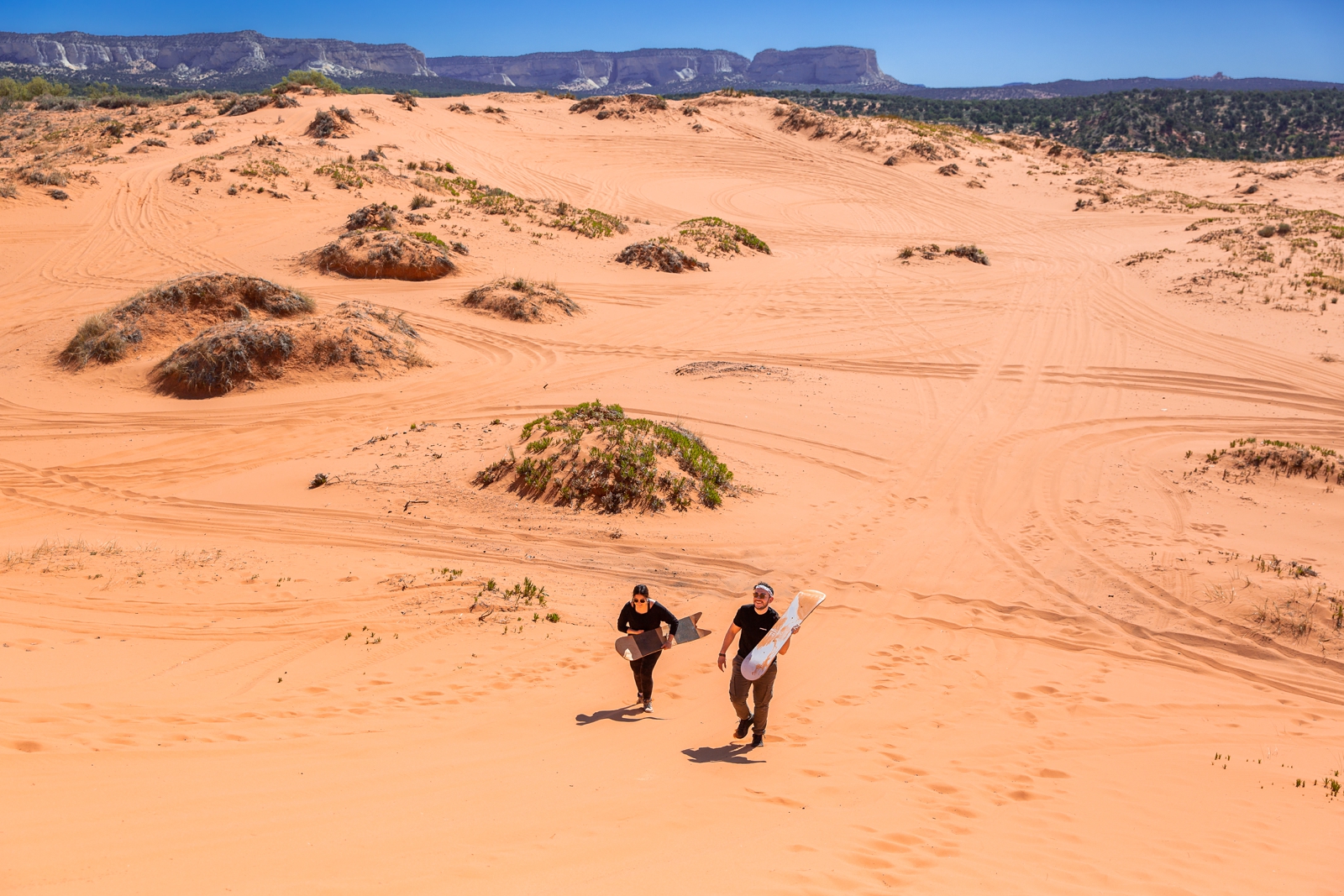 a newly engaged couple walking back up the sand hill after sandboarding down it by the Utah slot canyons