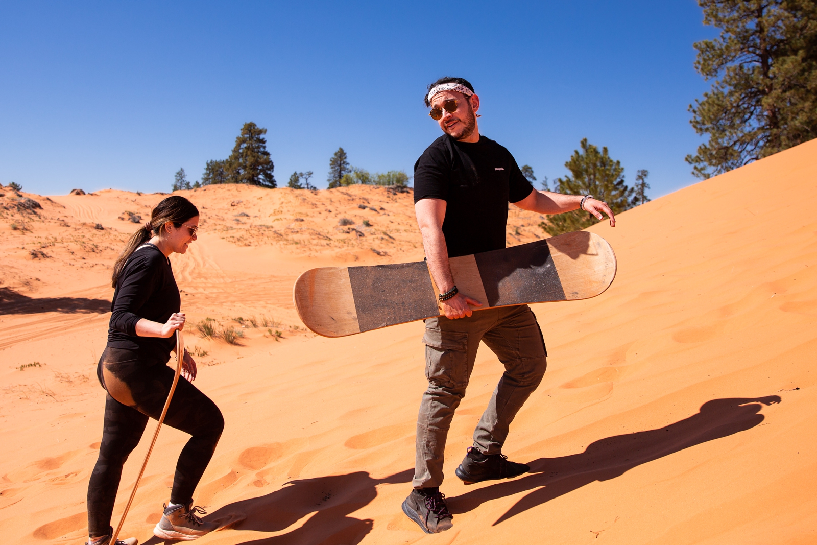 a newly engaged couple walking back up the sand hill after sandboarding down it by the Utah slot canyons