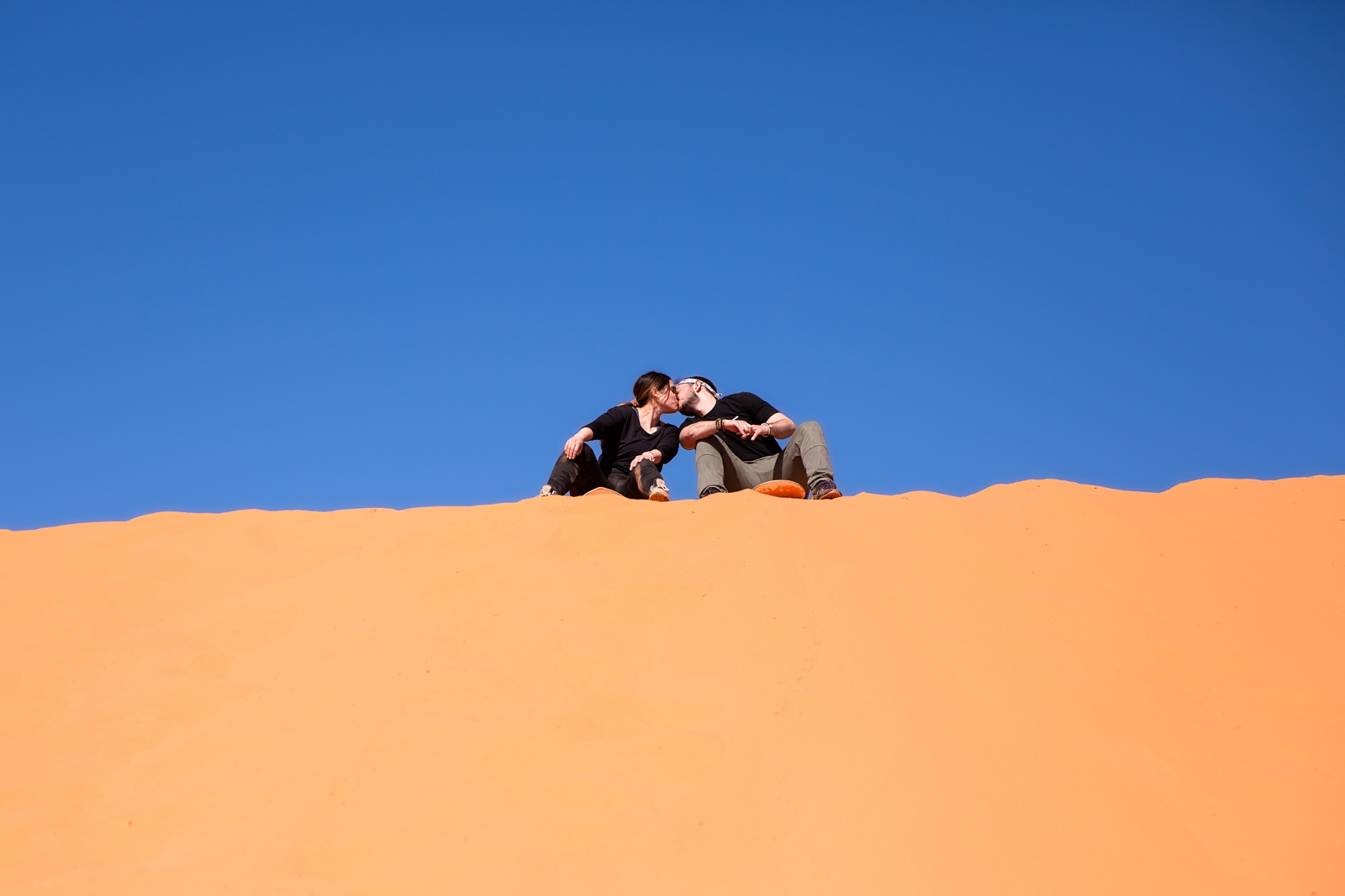 a newly engaged couple posing on their sandboards kissing before going down the hill by the Utah slot canyons