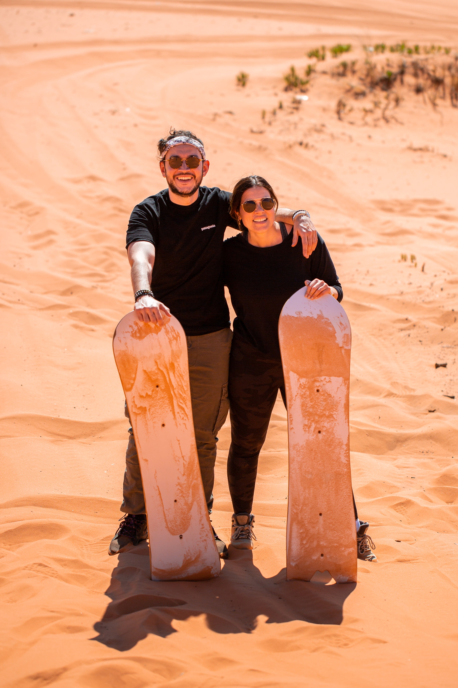 A newly engaged couple posing and smiling with their sandboards by the Utah slot canyons