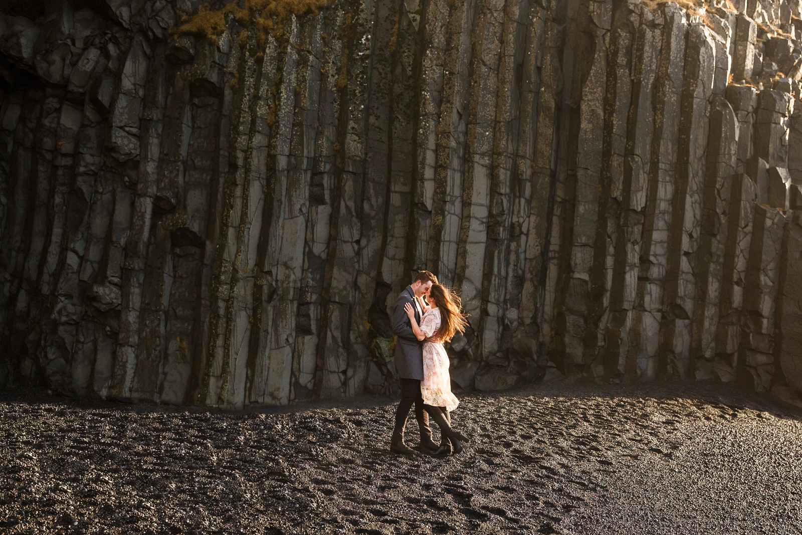 Engaged Couple looking at each other and snuggling by the basalt columns at their destination Iceland engagement session near Vik, Iceland