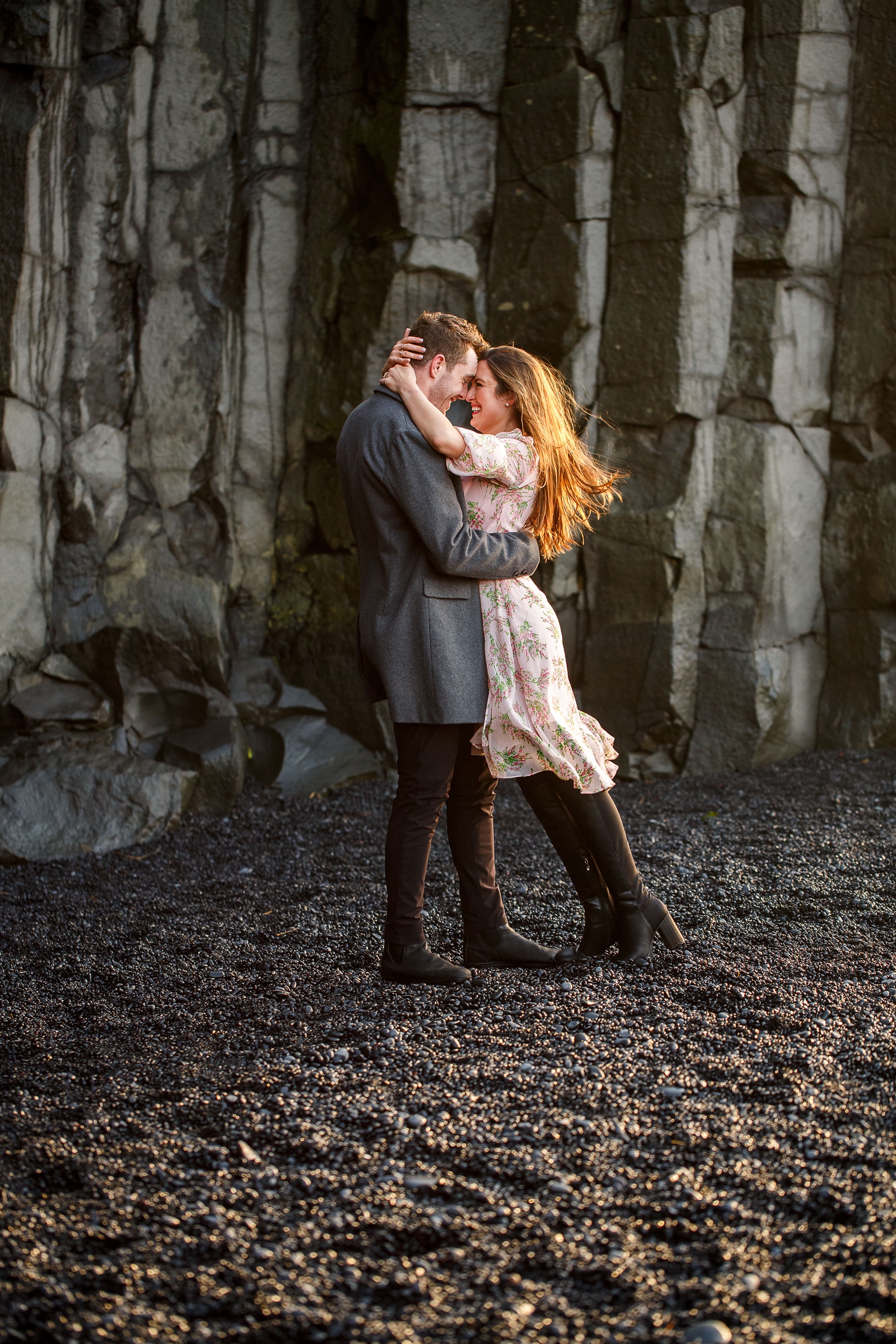 Smiling Couple holding each other and snuggling by basalt columns at their destination Iceland engagement session near Vik, Iceland