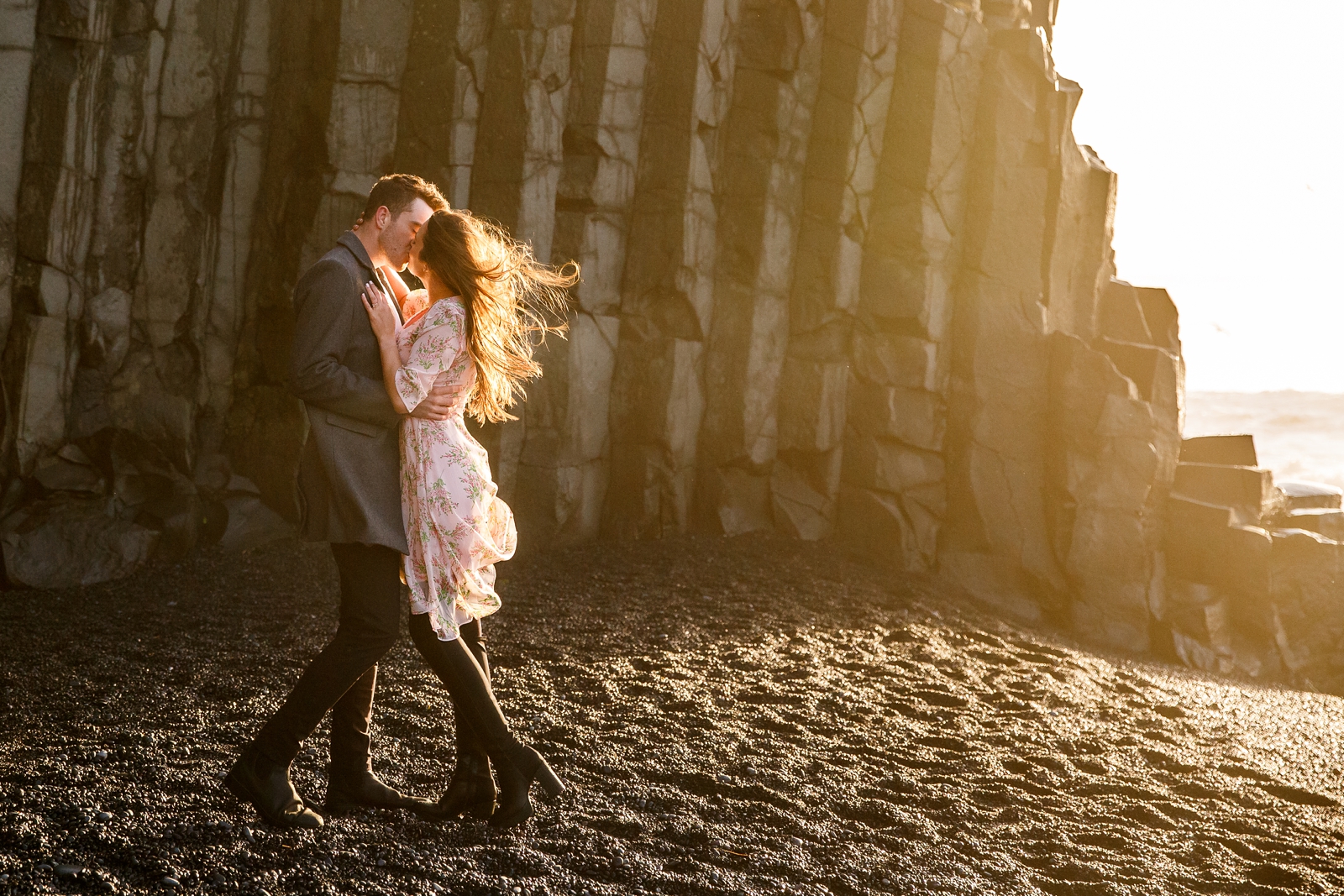 Smiling Couple kissing each other and snuggling by basalt columns at their destination Iceland engagement session near Vik, Iceland