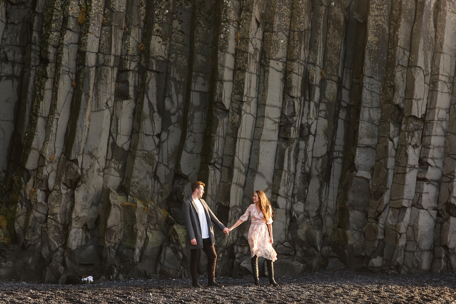Couple hand in hand looking at each other by basalt columns at their destination Iceland engagement session near Vik, Iceland