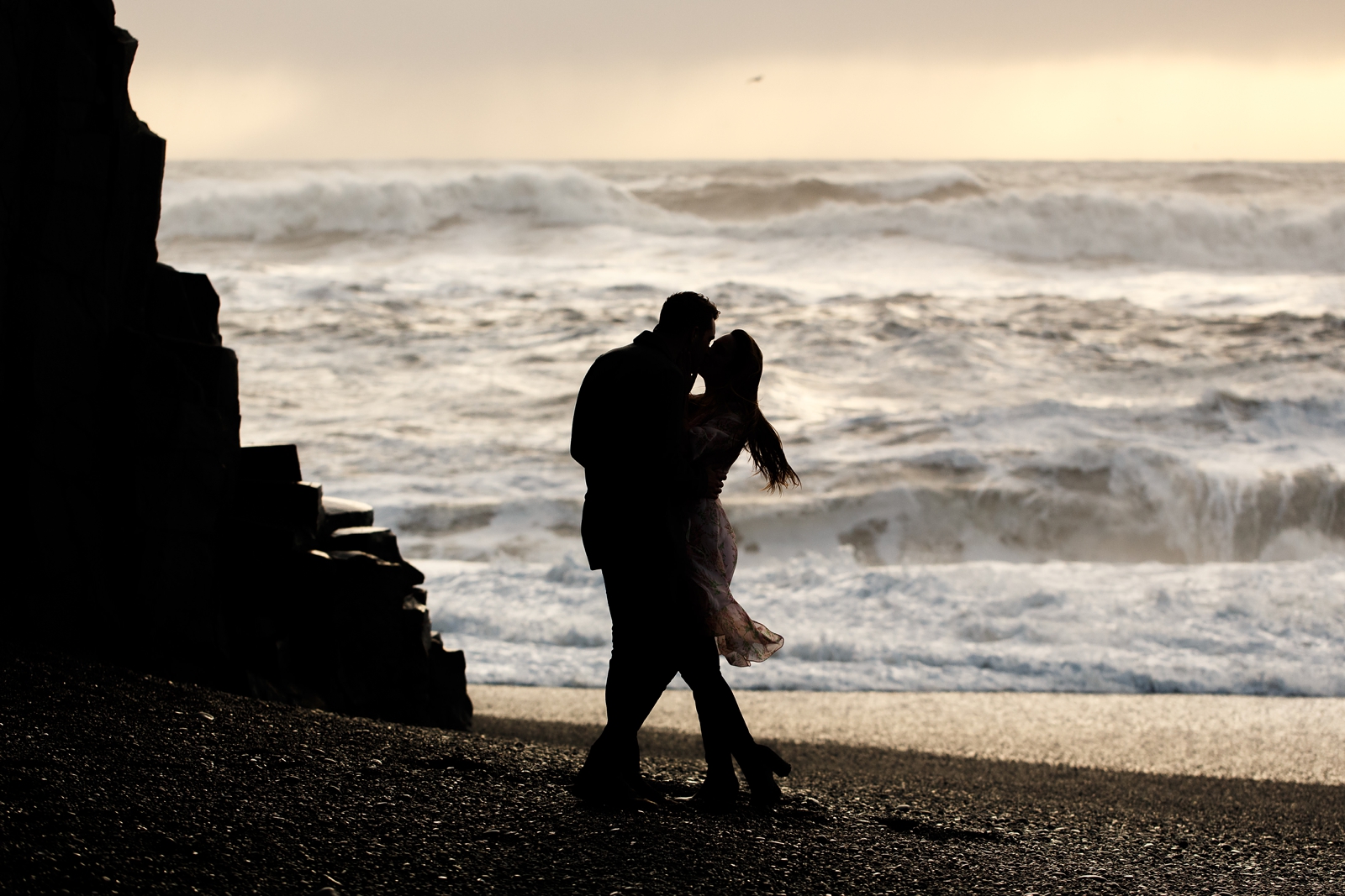 Silhouetted photo of Couple kissing each other by basalt columns with the ocean in the background at their destination Iceland engagement session near Vik, Iceland