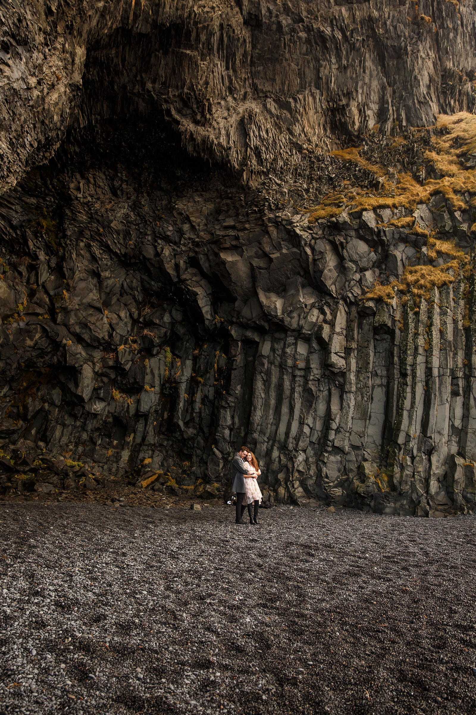 Wide photo of Engaged couple standing by basalt columns at their destination Iceland engagement session near Vik, Iceland