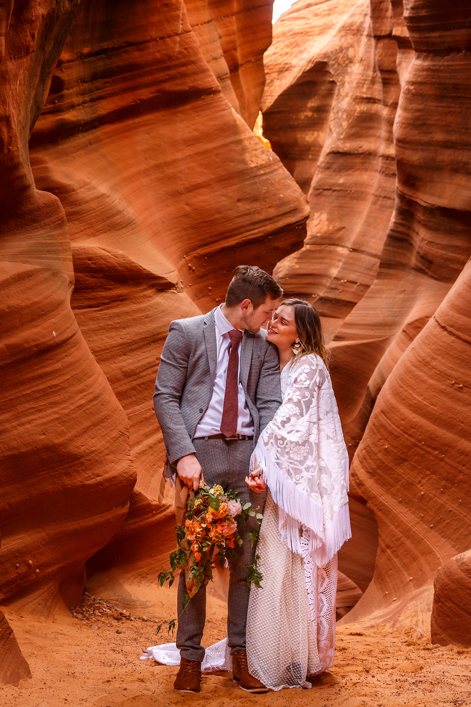 A boho in-love couple embracing during their red rock slot canyon elopement in Waterholes Canyon near Horseshoe Bend in Page Arizona