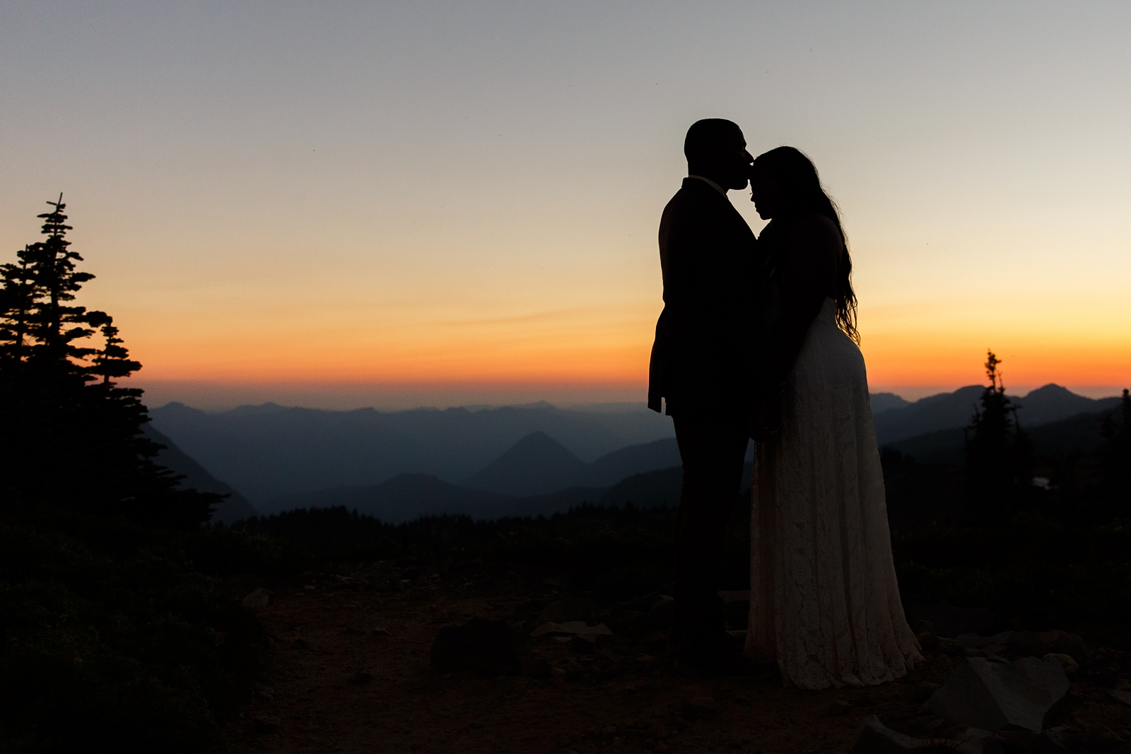An adventurous young couple embrace in front of the sunset at Mount Rainier National Park during their hiking elopement.