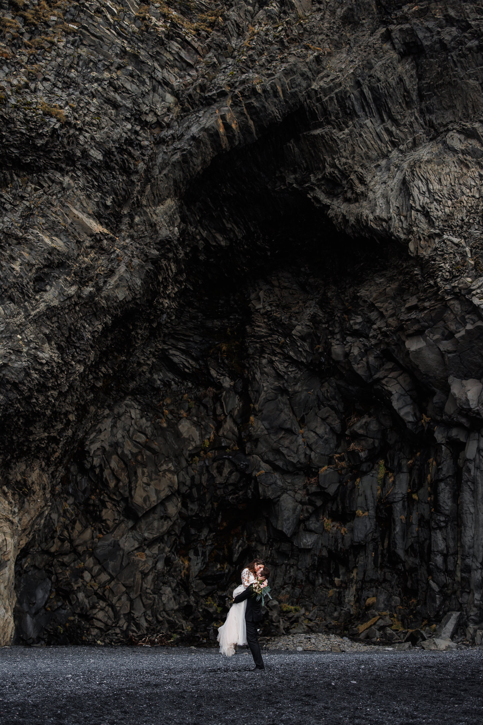 Couple embrace underneath the Basalt Columns of Reynisfjara, near Vik Iceland.