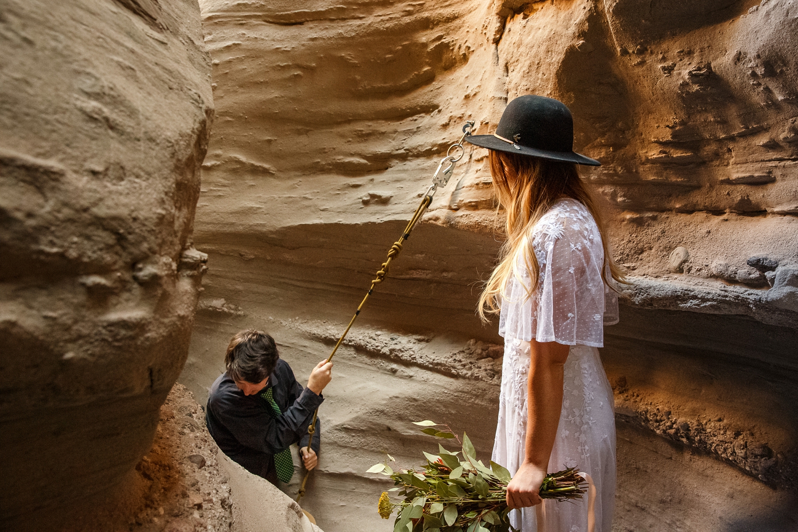 The Groom uses a rope to help him climb the rocky face of the canyon at this couple's slot canyon elopement.