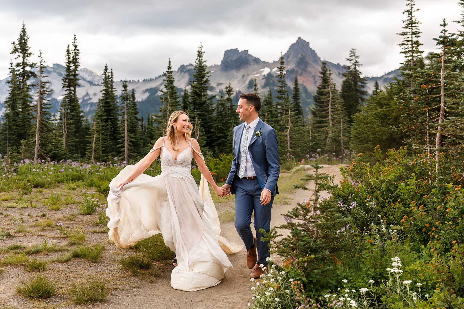This eloping couple runs down a trail in front of mountains in Mount Rainier NP.