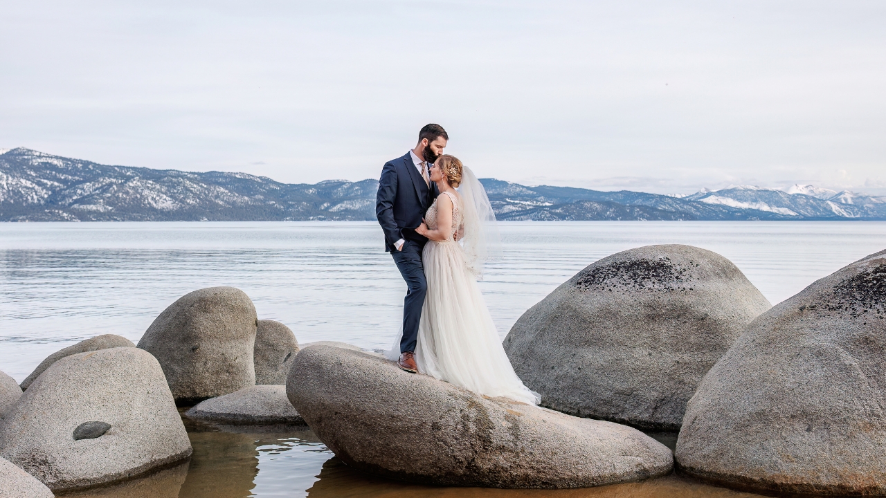 photo of groom kissing his bride on the forehead while standing on rocks with Lake Tahoe behind them