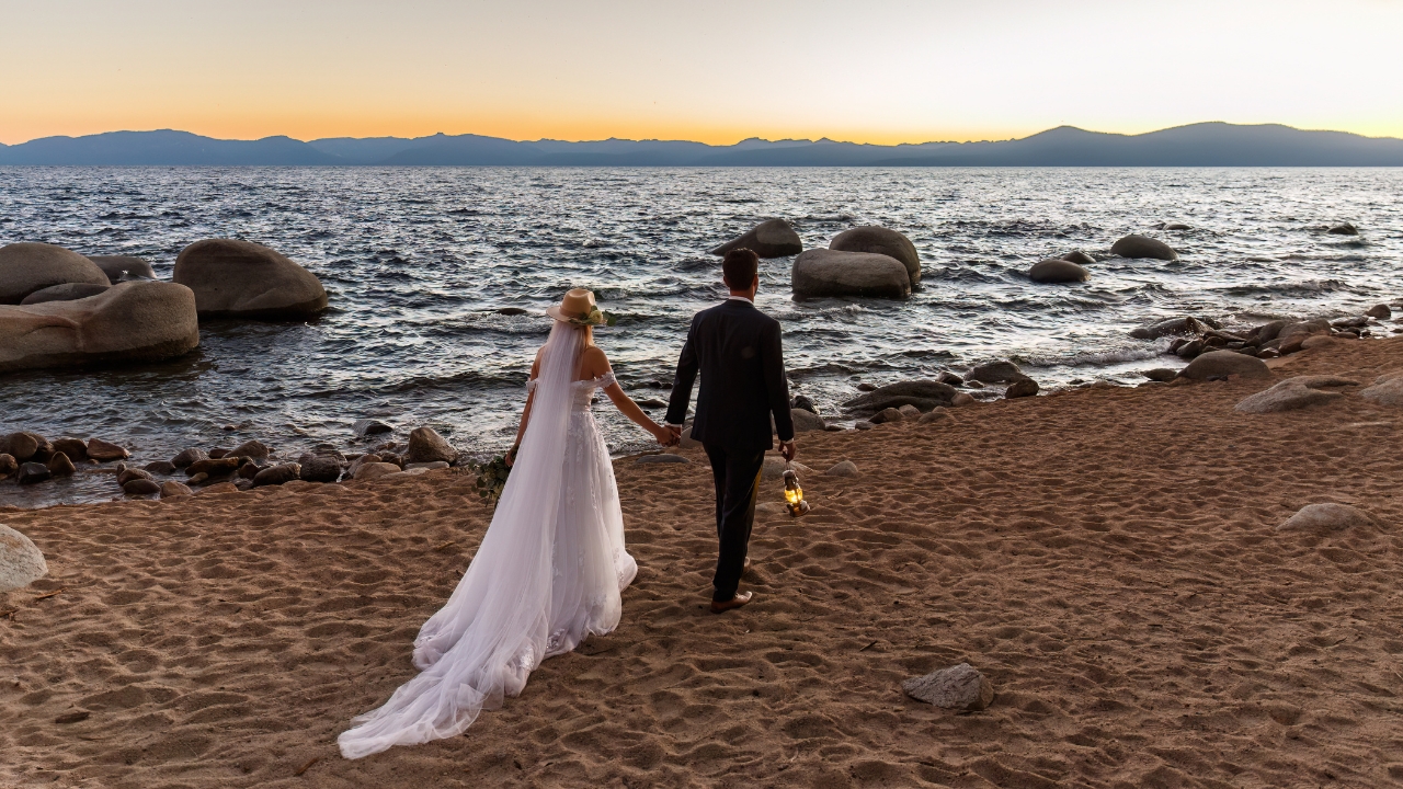photo of bride and groom walking towards Lake Tahoe with lanterns in their hands 