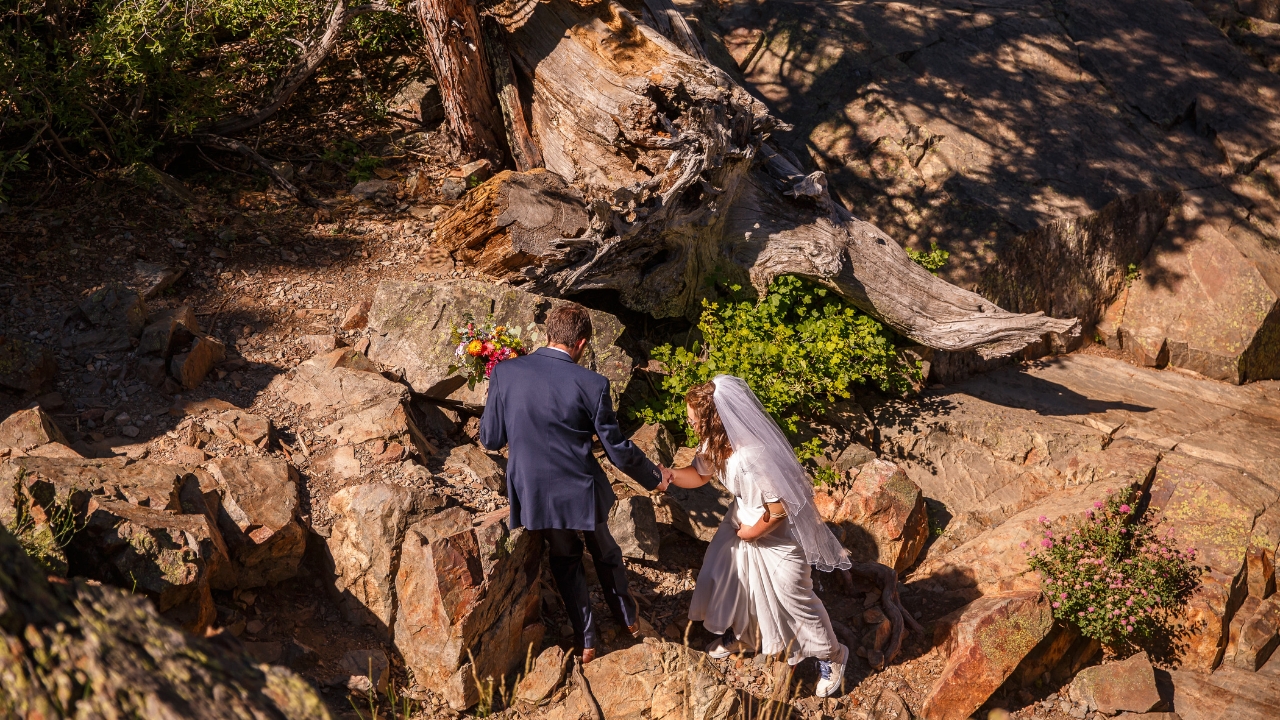 photo of groom helping his bride up a rock face on their wedding day