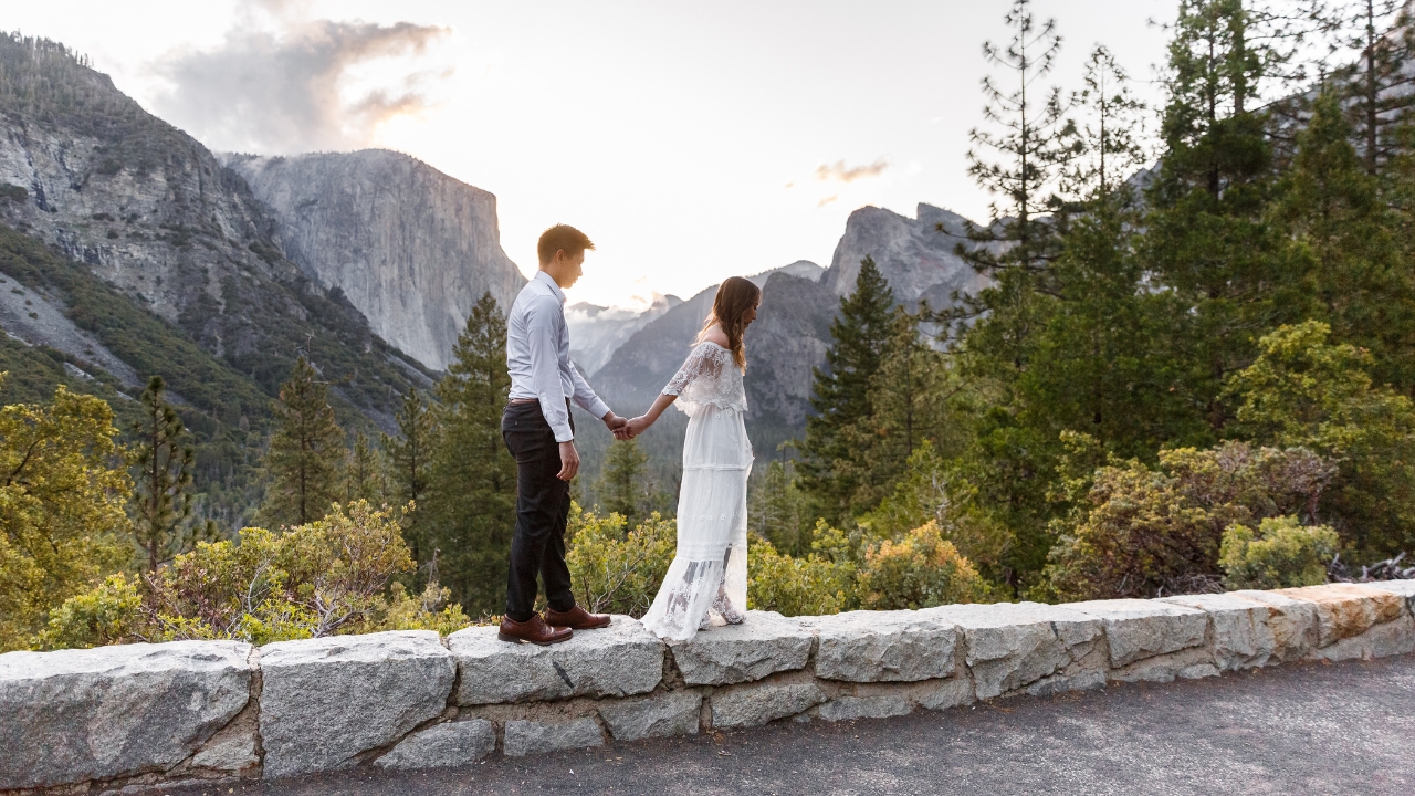 photo of bride and groom walking long ledge with Yosemite behind them