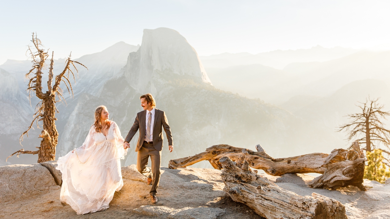 photo of bride and groom stepping over rocky ledge with Half Dome behind them at their elopement