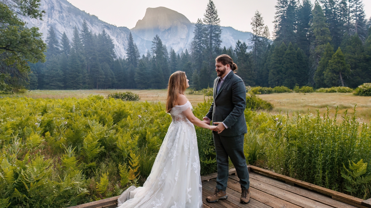 photo of bride and groom holding hands on wooden bridge with Half Dome behind them for their Yosemite elopement