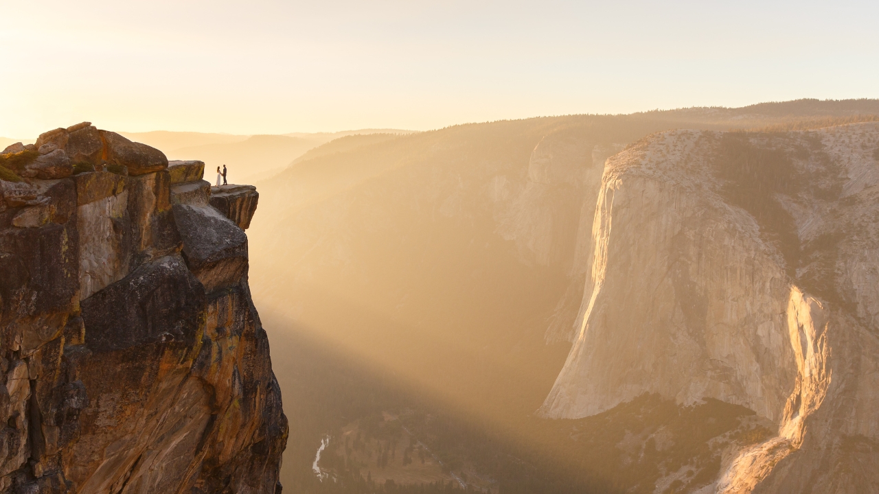 photo of bride and groom holding hands in the distance with the sun rising in Yosemite