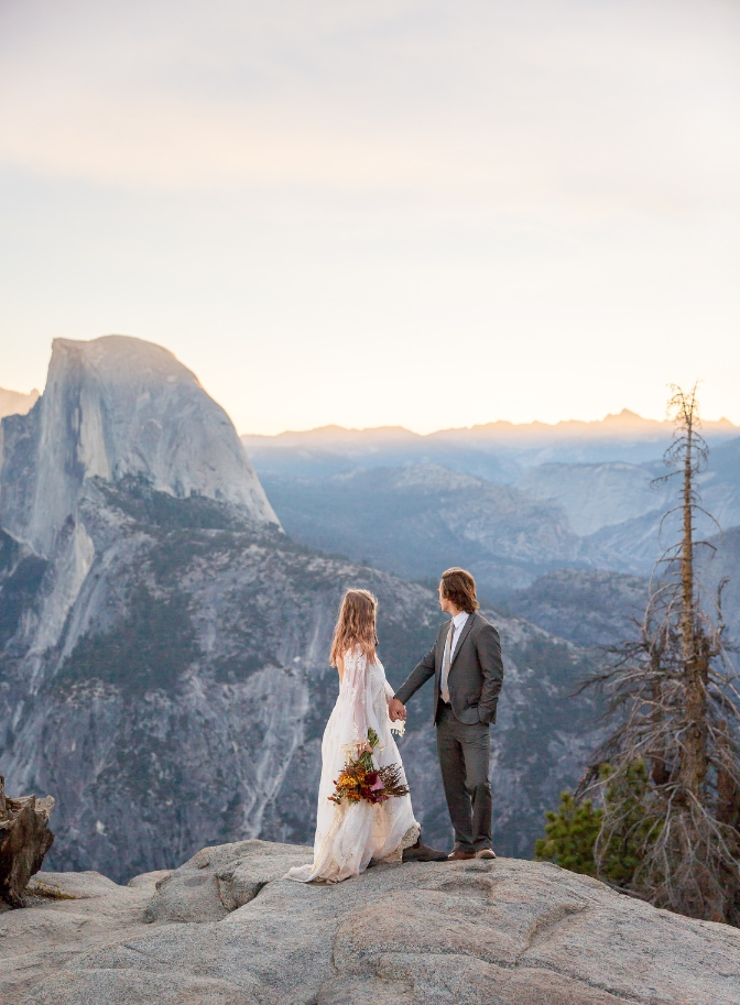 photo of bride and groom holding hands and looking back at Half Dome at Taft Point