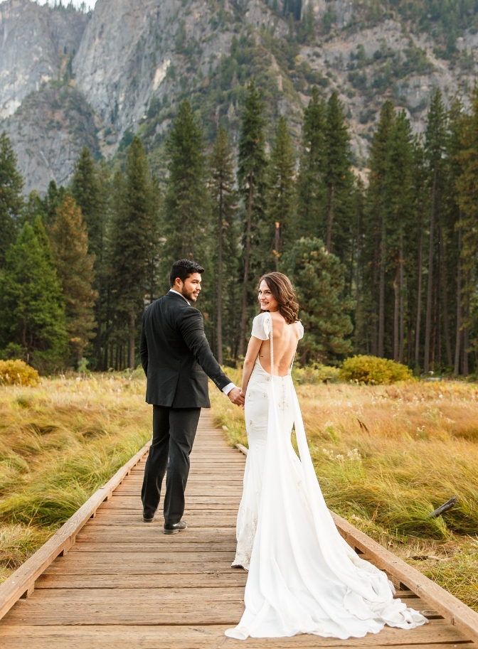 photo of bride and groom walking along wooden pathway and looking back