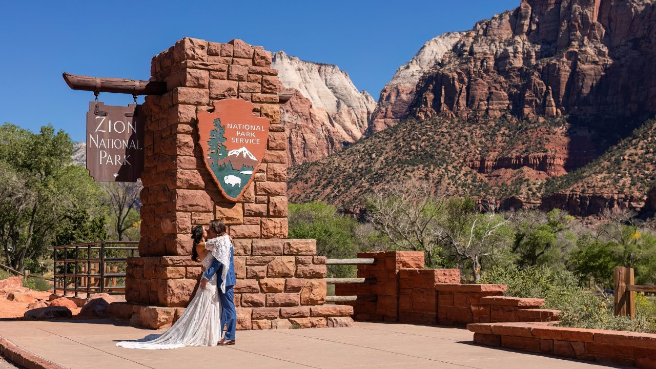 photo of bride and groom kissing in front of Zion National Park sign
