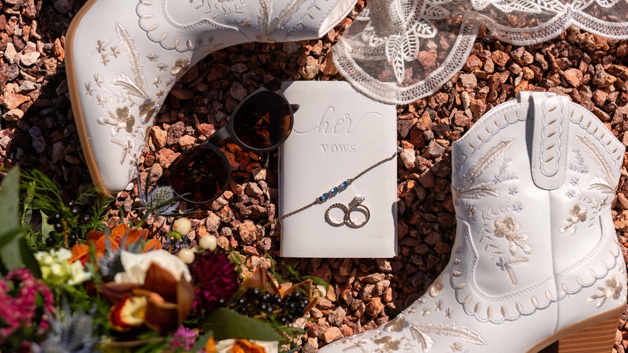 photo of bridal accessories: jewelry, boots, vow book, sunglasses, bouquet, and veil