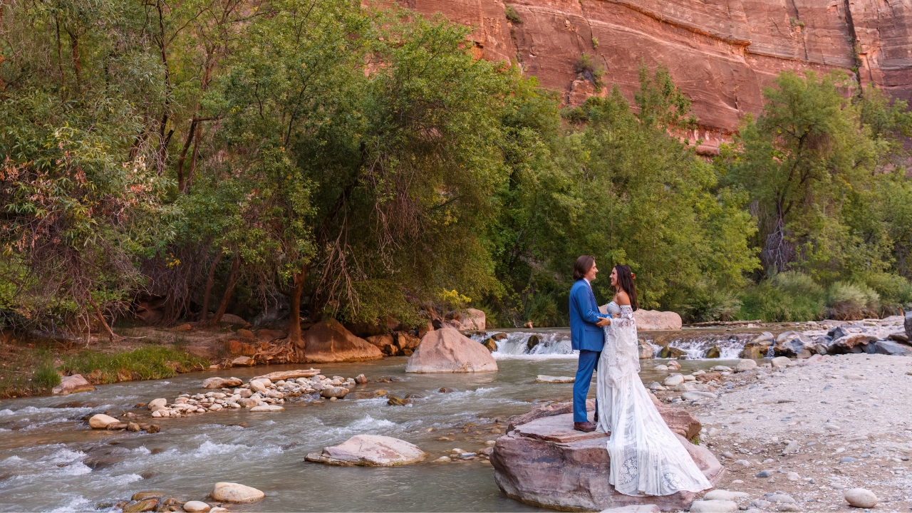photo of bride and groom standing on a rock, holding hands, with a waterfall behind them in Zion