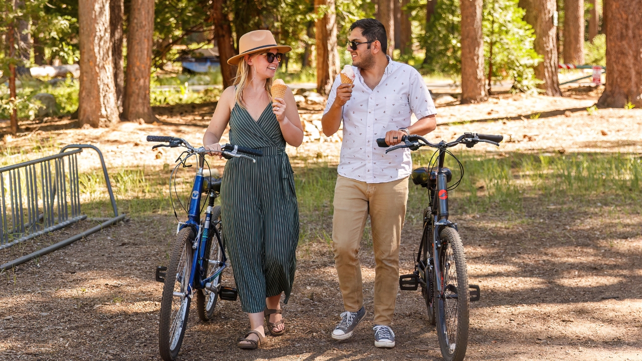 photo of couple holding ice cream cones and standing next to bike, smiling at each other