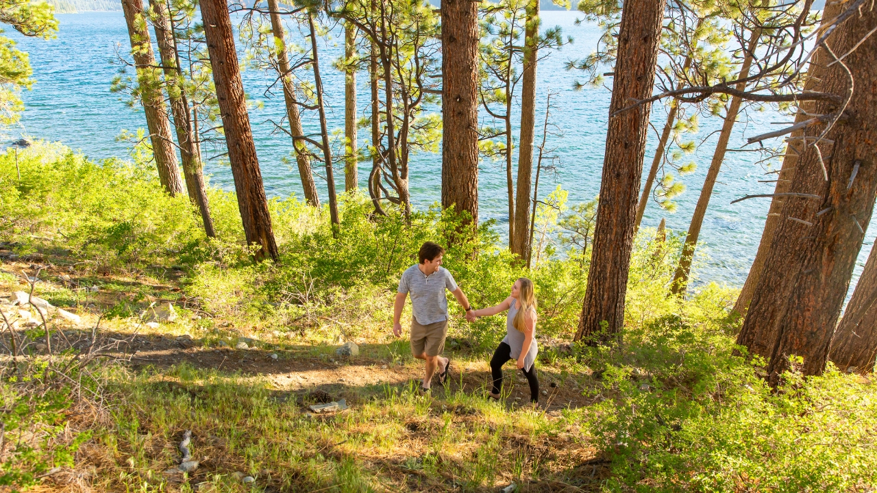 photo of couple holding hands while walking along a trail with a lake behind them